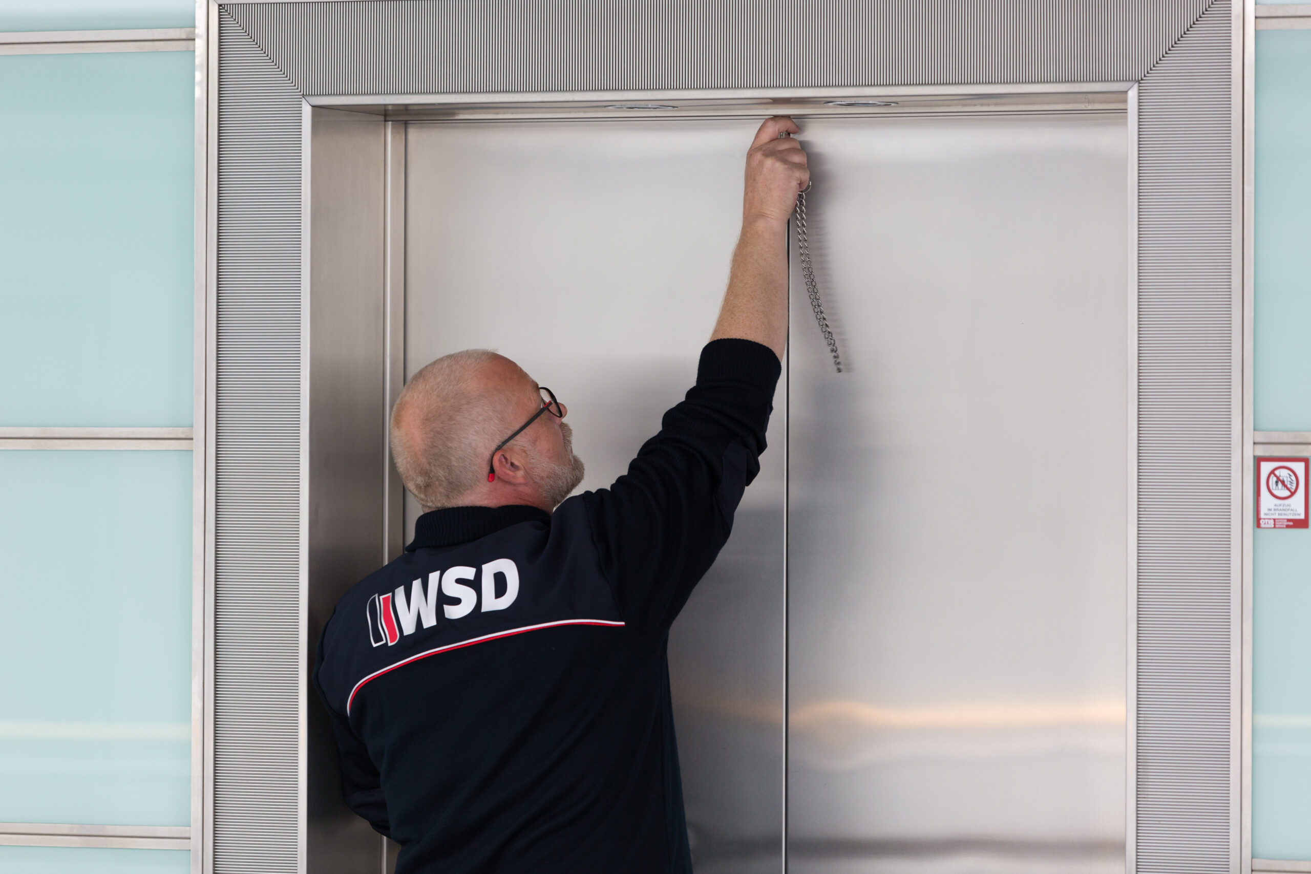 Mitarbeiter mit WSD-Logo auf der Kleidung überprüft eine Aufzugtür